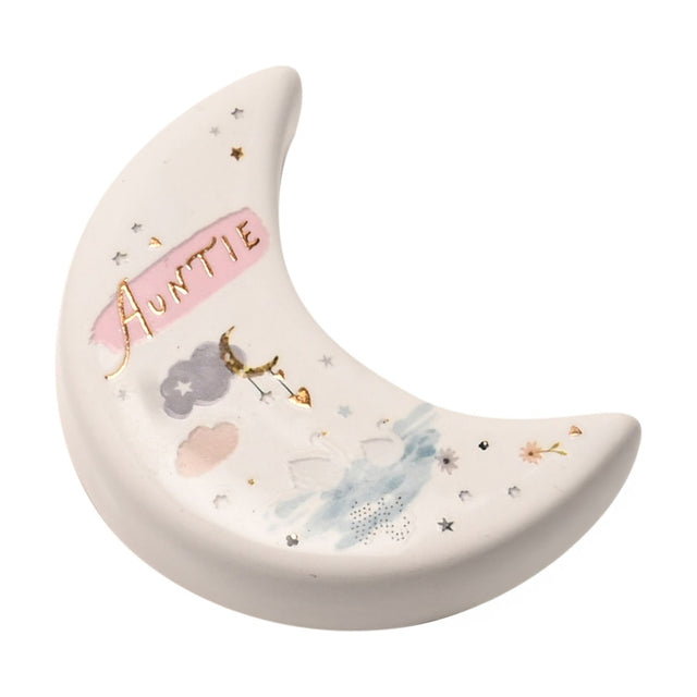 White ceramic crescent moon keepsake token reading "Auntie" in gold script, with pink banner, clouds, swans and stars in pink, grey and blue, on a white background.