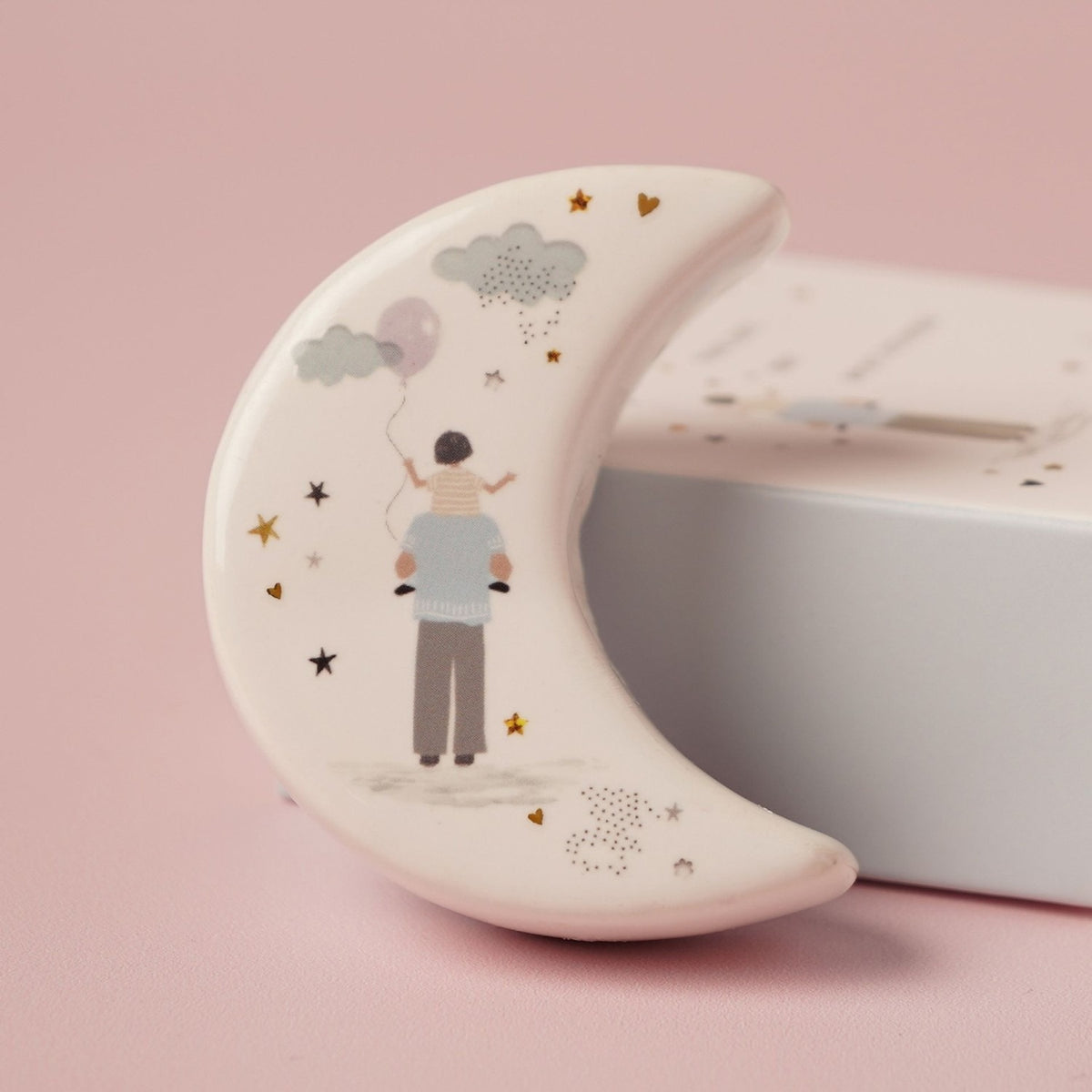 Daddy Crescent Moon Ceramic Token Match Keepsake Box in white, featuring a father carrying a child with a balloon, clouds, and gold star and heart details, shown beside its box on a pink background.