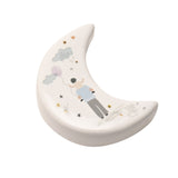 White ceramic crescent moon keepsake token featuring a figure holding balloons, with painted clouds, stars, and gold heart accents, set on a plain white background.