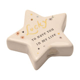 White ceramic star-shaped keepsake token with "Lucky to have you in my life" in gold and black lettering, decorated with small hearts, stars and flowers, on a plain white background.