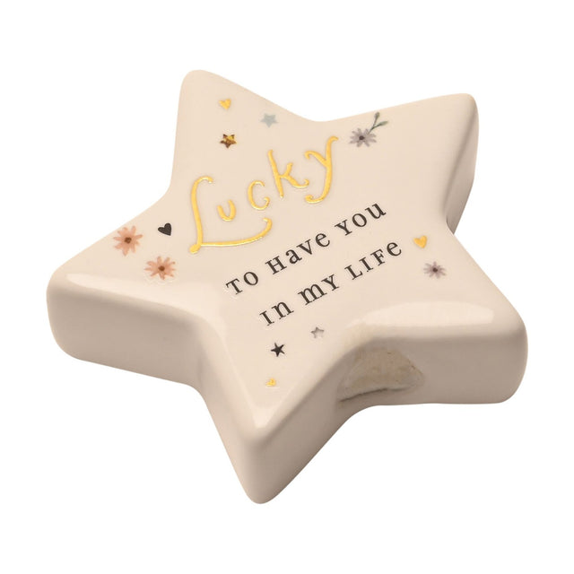 White ceramic star-shaped keepsake token with "Lucky to have you in my life" in gold and black lettering, decorated with small hearts, stars and flowers, on a plain white background.