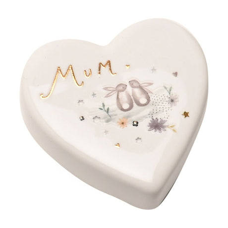 White glossy ceramic heart-shaped keepsake token reading "Mum" in gold script, decorated with two grey bunnies, pale flowers, leaves and gold stars, set on a plain white background.
