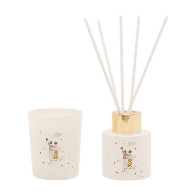 White glass mini candle and reed diffuser set with gold cap and white reeds, printed with a friends motif of hearts, stars and a cloud, on a plain background.