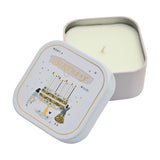 Square tin scented candle with white lid showing a birthday cake, two figures, stars and hearts, "Make a Birthday Wish" text, lid open beside the pale candle on a white background.