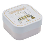 Square tin scented candle with white lid featuring a gold-lined "Make a Birthday Wish" design, layered cake, candles, stars and hearts, set on a pale pink base, plain white background.