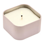 Lit square scented candle in a pale purple tin with white wax and a cotton wick, shown lidless on a plain white background.