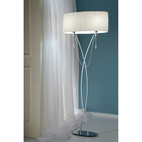 The Lucca 2 Light Crystal Floor Lamp features a chrome base and white shade, offering modern, dimmable lighting near a window with sheer curtains and enhancing the contemporary look against a blue wall.