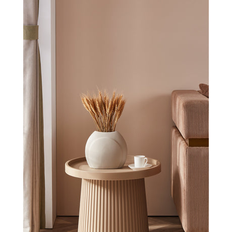 Lyaglan ceramic vase in matt beige with a rounded, pebble-like body, holding dried wheat stems on a ribbed side table in a living room setting.