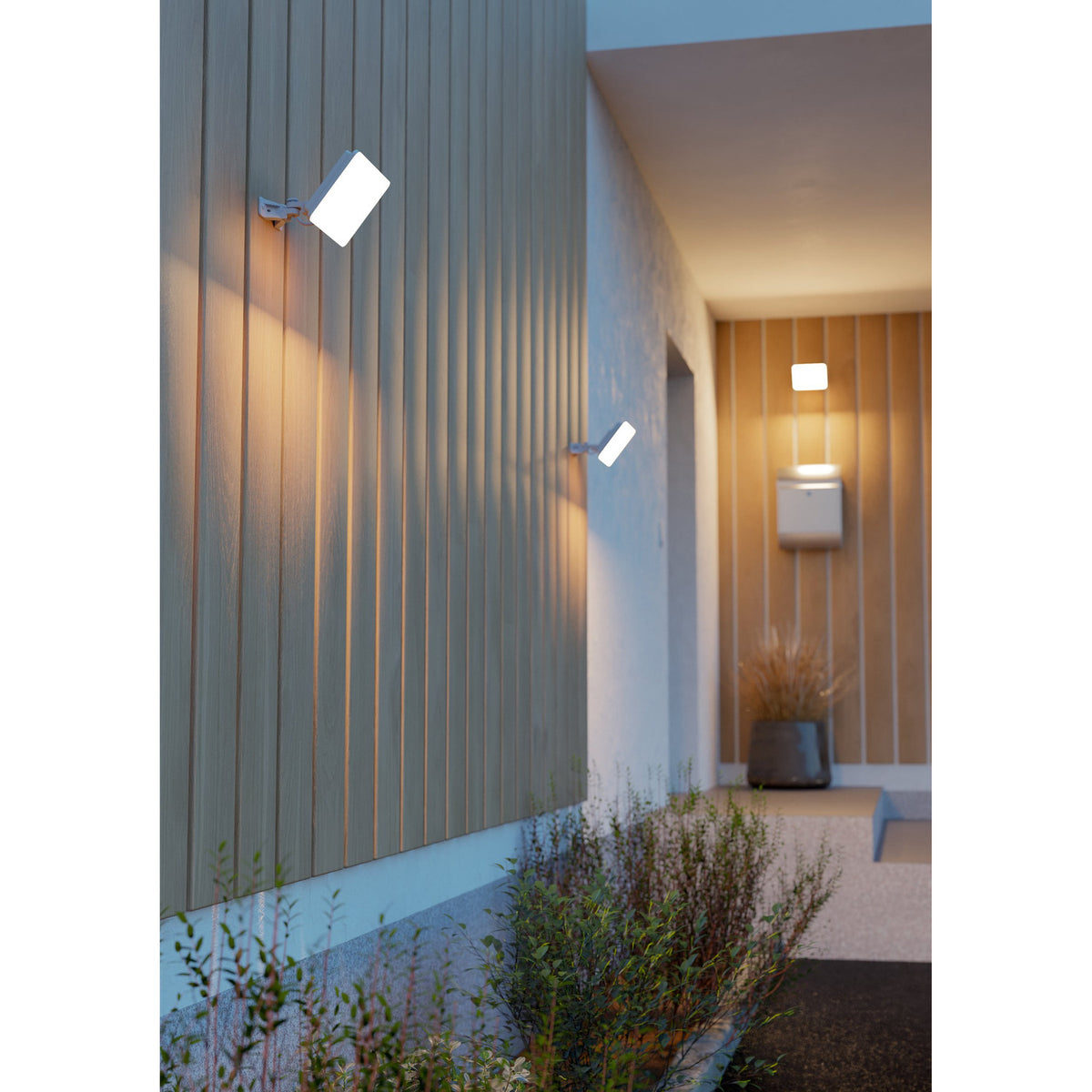 Machio LED Flood Light 30W in white mounted on wooden slatted exterior walls either side of a hallway, casting warm downward light near an entrance with plants.