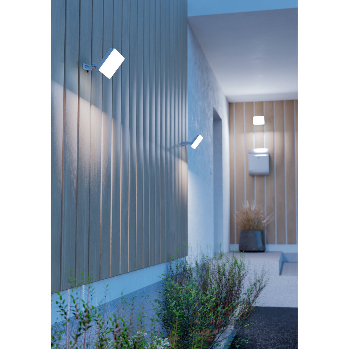 Machio LED Flood Light 30W in white mounted on wall brackets outside a modern home, illuminating slatted wood panelling along an entrance walkway.