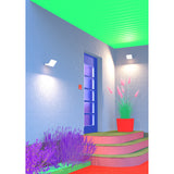 White LED wall-mounted floodlight with rounded rectangular aluminium body, illuminating a covered outdoor entrance beside a blue front door and potted plant.