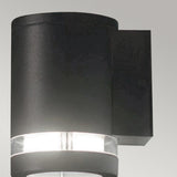 The Magnus 1 Light Outdoor Wall Light in graphite boasts a modern, sleek cylindrical design, complete with a frosted glass section that emits soft white light. Rated IP44, it is an ideal fixture for enhancing your exterior space.