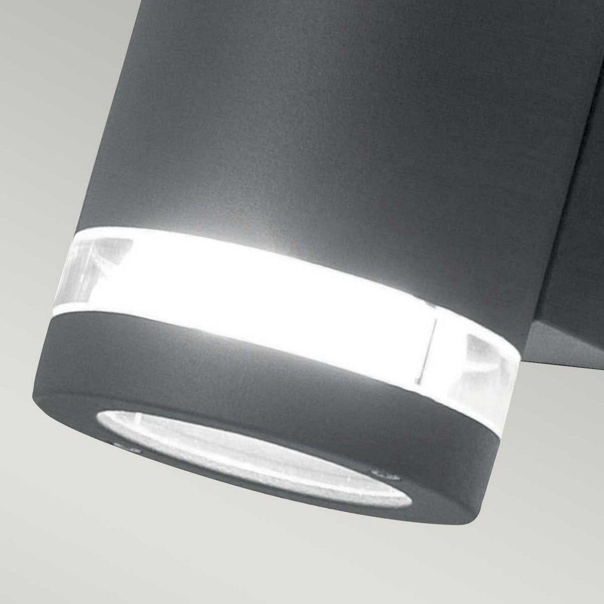Close-up of the Magnus 2 Light Outdoor Wall Light in graphite, highlighting its modern cylindrical design with an illuminated white ring. Set against a pale gray background, this fixture exudes a sleek and minimalist aesthetic.