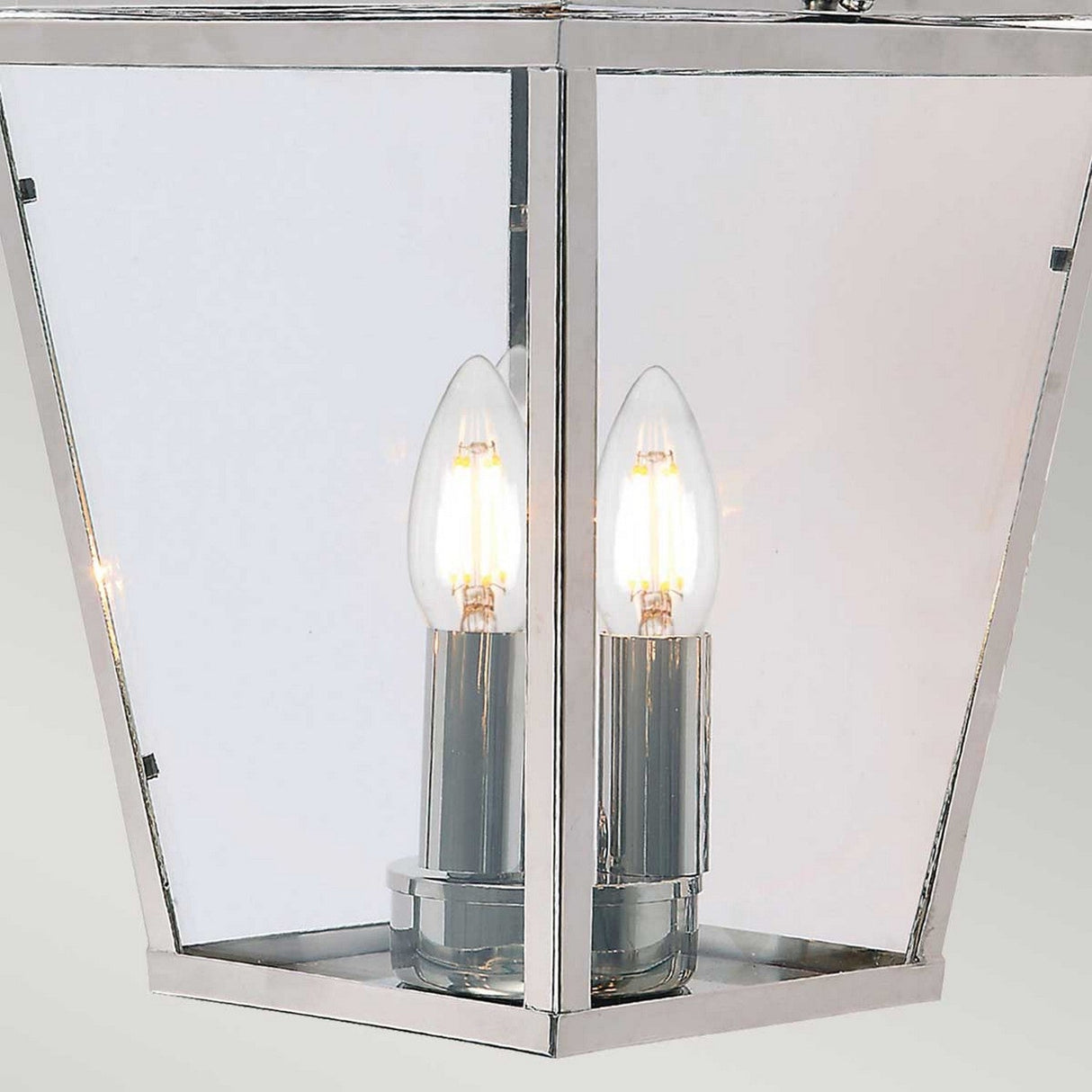 A close-up of the Mansion 3 Light Outdoor Chain Pendant in polished nickel, featuring a lantern-style design with three exposed, glowing bulbs. This fixture showcases a sleek, modern aesthetic with a harmonious blend of glass and polished nickel finishes.