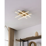 Marinello 1 LED flush ceiling light with four black bars crossed over a square wood plate, illuminated in warm white on a white ceiling above a shelf styled with books and decor.