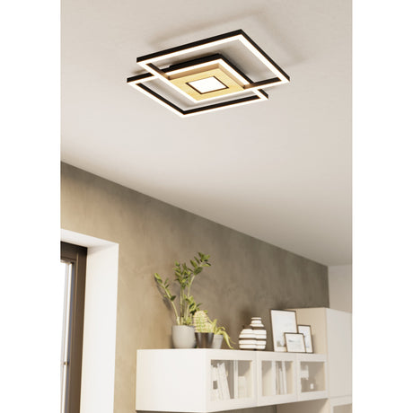 Marinello LED flush ceiling light mounted at an angle, with overlapping black square frames and a brown wood-grain centre panel, shown above a hallway cabinet with decor.