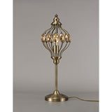 The Marisa 1 Light Crystal Table Lamp in antique brass with amber crystal accents stands on a plain surface, showcasing its vintage-inspired openwork metal shade and round base against a neutral gray background.