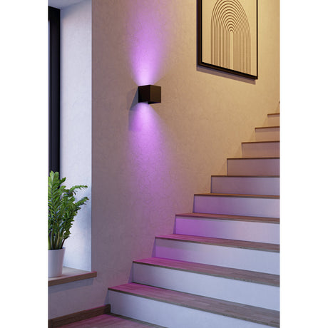 Masmena square LED outdoor wall light in matt black aluminium, mounted on a staircase wall and casting up and down beams in RGB purple over the stairs.