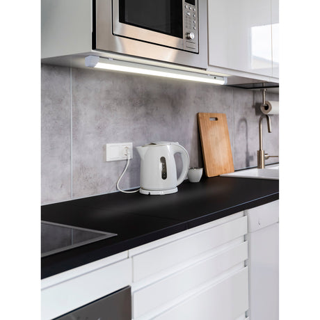 Mattanza white LED flush ceiling light, 120cm slim linear strip, mounted under a kitchen cabinet above a worktop with microwave and kettle.