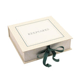 Square cream keepsake box with "KEEPSAKES" lettering on the lid, a floral border, leafy-patterned sides, and a deep green ribbon tied in a bow, on a plain white background.