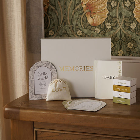 Cream Memories keepsake box with gold lettering and floral sides, displayed with a BABY booklet, LOVE pouch, hello world card, and stacked keepsake boxes on a wooden dresser.