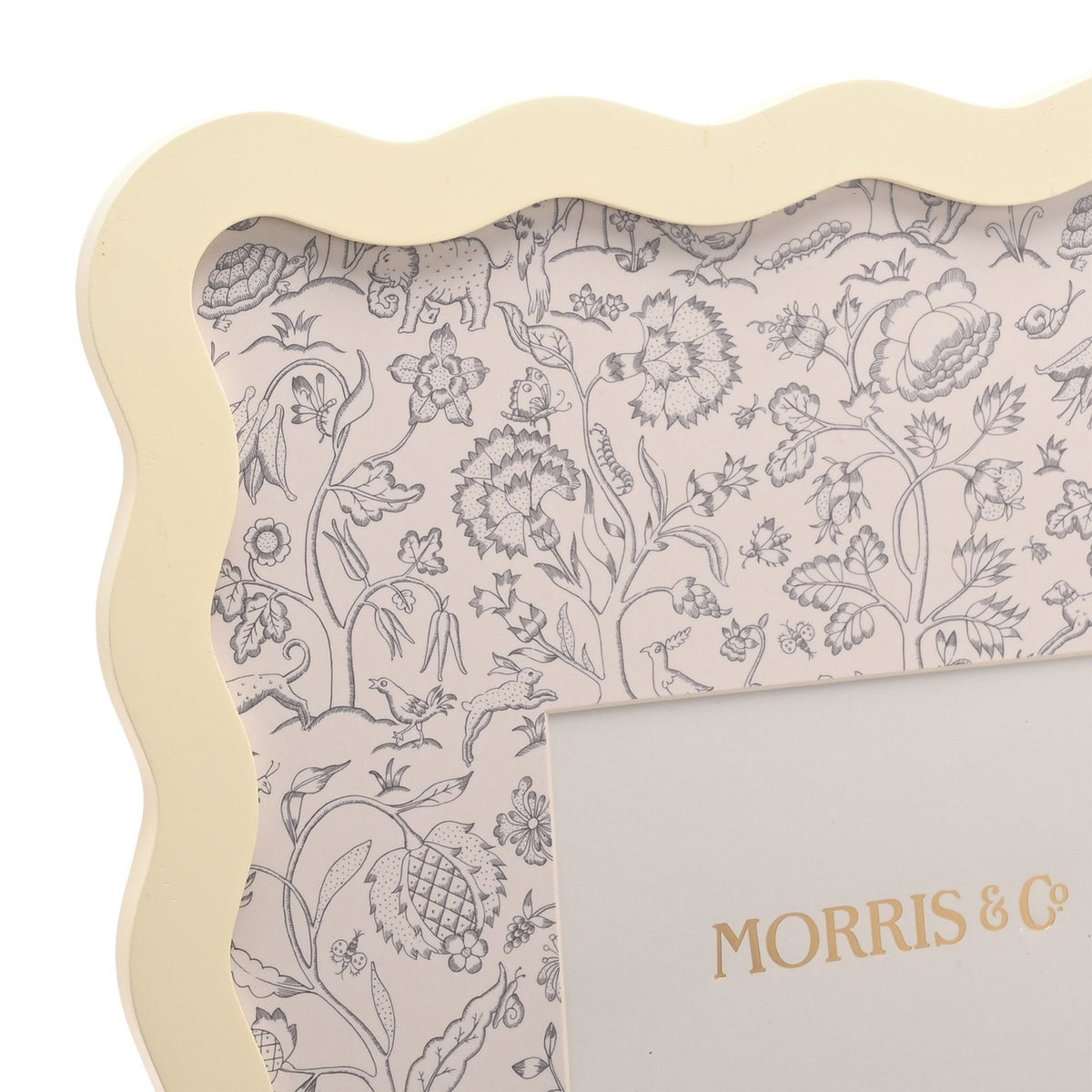 Close-up of the Baby Wiggle Metal Photo Frame in cream with a wavy scalloped border, showing a botanical mount with grey line drawings of flowers, birds and animals around a rectangular opening.