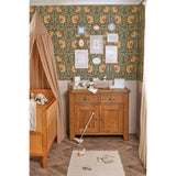 Cream metal photo frame with wavy scalloped border and botanical-print mount, displayed on a wooden sideboard in a nursery setting.