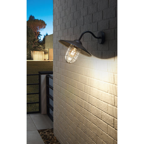 Melgoa Outdoor Wall Light in black, with gooseneck arm, wide hood and cage-wrapped glass diffuser, illuminated on a brick wall beside a patio at dusk.