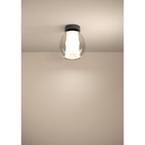 Menorca LED flush ceiling light with black nickel steel canopy and egg-shaped clear glass shade over a white satin glass inner cylinder, illuminated on a neutral ceiling.