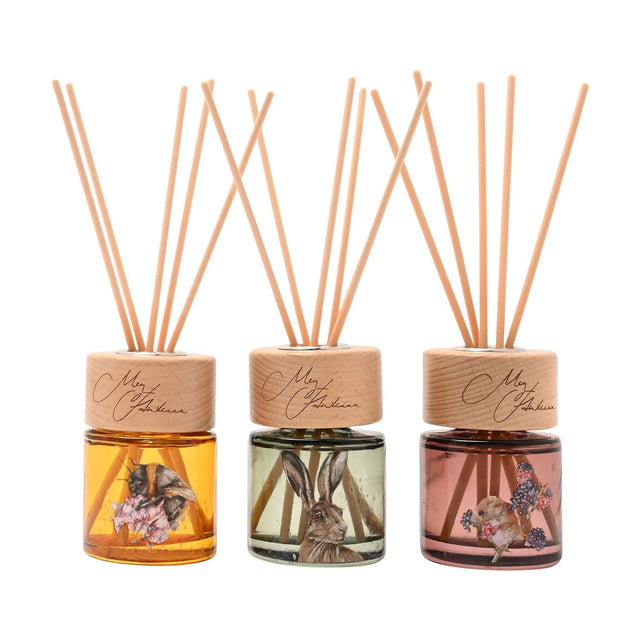 Set of three mini reed diffusers with wooden caps and reed sticks, featuring amber, sage green, and dusty pink glass bottles illustrated with a bee, hare, and mouse, on a white background.