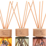 Set of three mini reed diffusers with wooden caps and reeds, featuring amber, sage green, and dusty pink glass bottles illustrated with a bee, hare, and mouse.