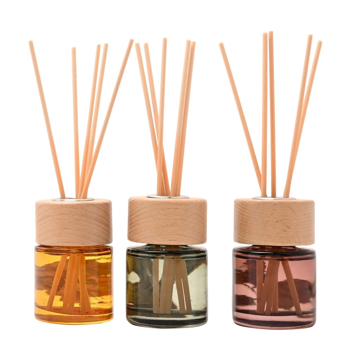 Set of three mini reed diffusers in amber, sage green, and dusty pink glass bottles with wooden collars and reed sticks, set against a plain white background.