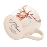 Off-white ceramic cup shown on its side, featuring a watercolour stag's head with antlers in russet tones, paint splashes, and a signature on the base, set against a plain white background.