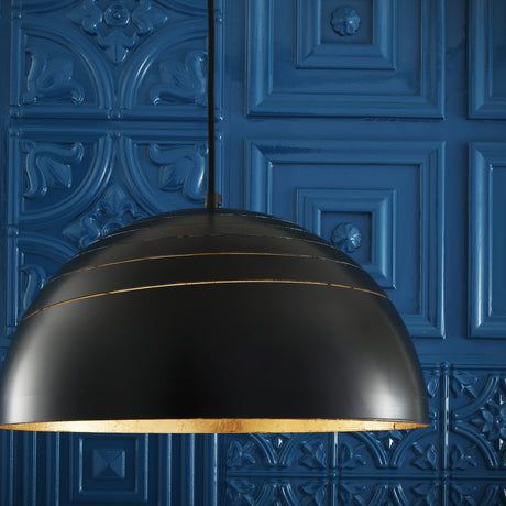 Midas dome pendant light in matt black steel with a gold leaf lined interior, showing ringed slot details, hung against a dark blue patterned panel wall.