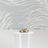 Take a closer look at the Milo 1 Light Table Lamp, featuring a white ceramic base paired with an aged brass lamp holder. The light gray lampshade is beautifully adorned with a textured, embroidered pattern that resembles abstract fern leaves.