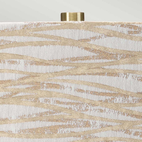 A detailed view of the Milo 1 Light Table Lamp reveals a decorative surface featuring an abstract pattern of wavy beige and white lines. The intricate texture shimmers subtly, paired with a partially visible cylindrical cap crafted from aged brass, accentuating its role as an elegant table lamp.