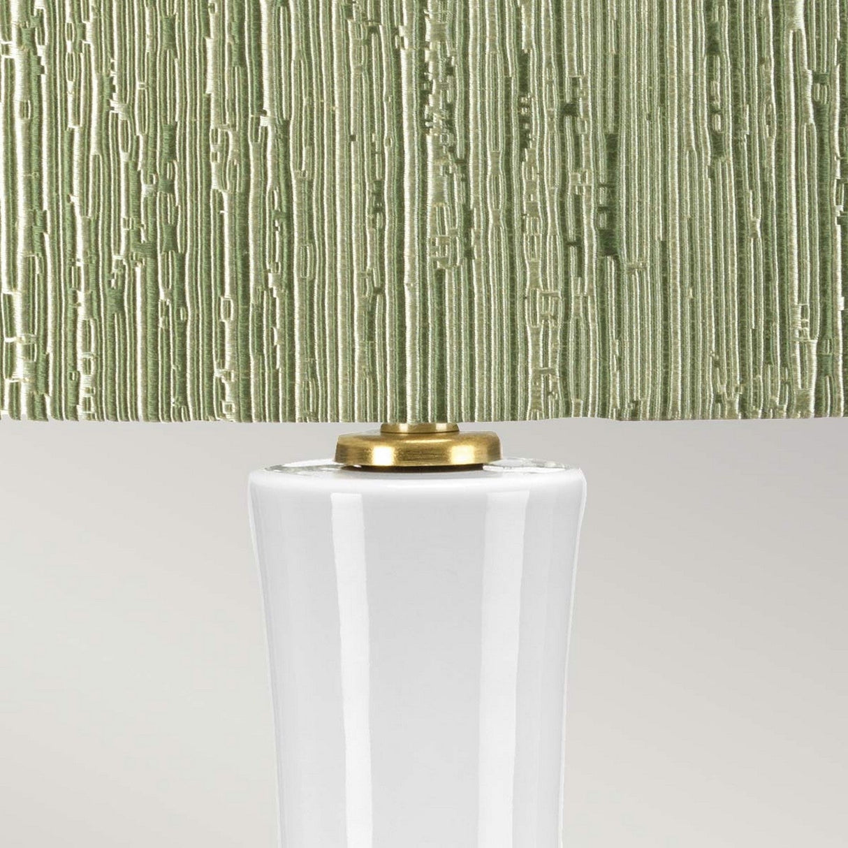 A close-up view of the Milo 1 Light Table Lamp highlights its textured, olive-green lampshade with vertical grooves, beautifully complemented by aged brass accents that elegantly connect the shade to a smooth, glossy white ceramic base.