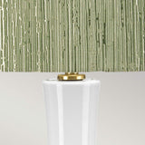 A close-up view of the Milo 1 Light Table Lamp highlights its textured, olive-green lampshade with vertical grooves, beautifully complemented by aged brass accents that elegantly connect the shade to a smooth, glossy white ceramic base.
