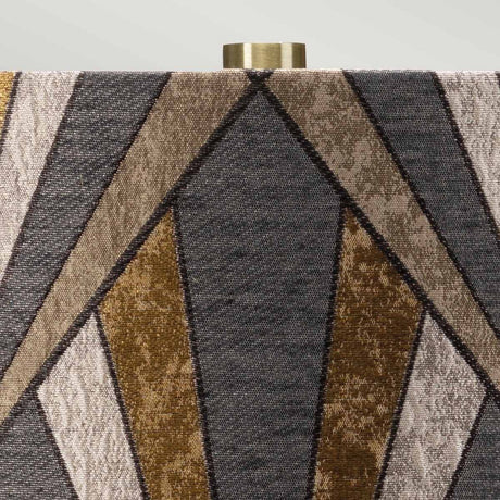 Close-up of the lampshade on the Milo 1 Light Table Lamp - Aged Brass/Brass, featuring a geometric pattern with triangular shapes in various shades of brown and gray. The top has an aged brass fitting that perfectly complements its elegant ceramic base.