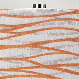 Close-up of the Milo 1 Light Table Lamp showing an abstract fabric design with an orange shade and silver wavy lines on a white backdrop. The top edge features a metallic cylindrical cap with a polished nickel finish, partially visible.