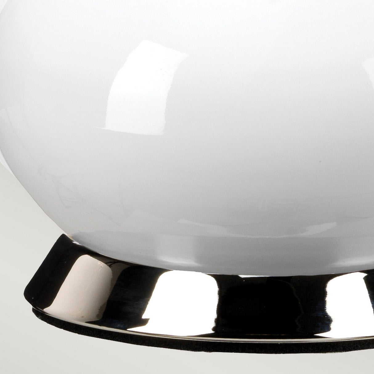 A close-up of the Milo 1 Light Table Lamp showcases its sleek, modern design, featuring an eye-catching reflective polished nickel base. The lamp's smooth white globe casts subtle light reflections, beautifully contrasting with its optional orange shade for a minimalist aesthetic.