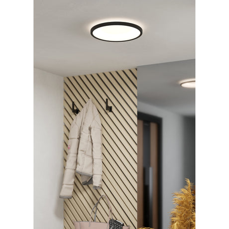 Minerario 30cm round LED flush ceiling light with black frame and white diffuser, shown installed in a hallway with a reflective mirror alongside a wood-slat wall and coat hooks.