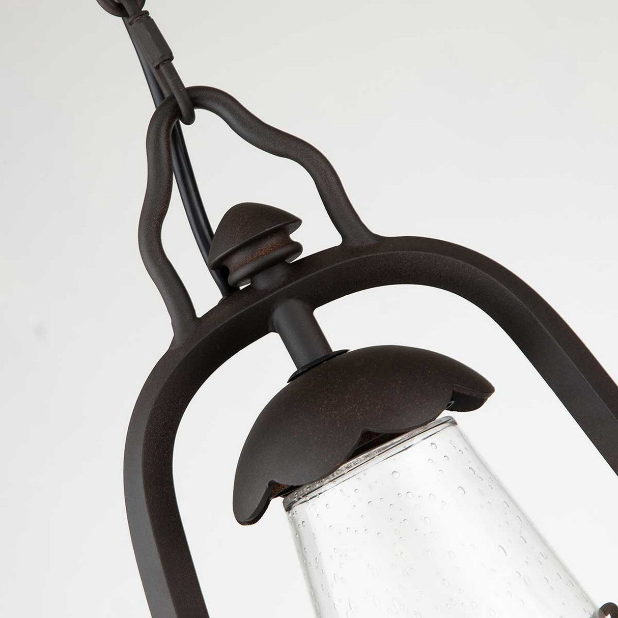 Close-up of the Miners 1 Light Outdoor Chain Pendant in old bronze, featuring a dark metal frame and clear, textured glass shade. This vintage lantern design showcases rustic, curved metal elements and an overhead hook, reminiscent of classic bronze fixtures, set against a plain light background.