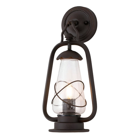 The Miners 1 Light Outdoor Wall Light in Old Bronze boasts a vintage-style design with an Old Bronze metal frame and clear glass shade. The exposed bulb within accentuates the circular metal details around the glass, offering a timeless charm.