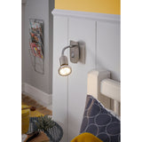 Mini 4 plug-in spotlight in satin nickel and chrome with gooseneck arm and GU10 bulb, shown mounted above a bedroom headboard with warm white light on.