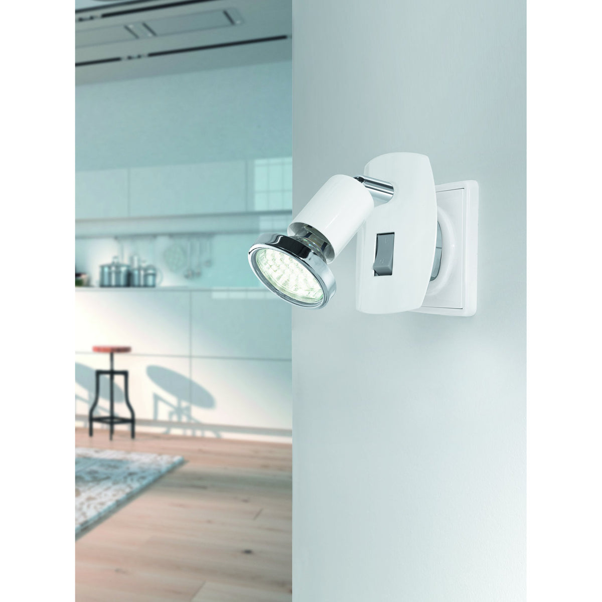 Mini 4 plug-in spotlight in white steel with chrome arm and ring detail, rocker switch on back plate, GU10 warm white bulb, shown on a wall in a kitchen setting.