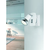 Mini 4 plug-in spotlight in white steel with chrome arm and ring detail, rocker switch on back plate, GU10 warm white bulb, shown on a wall in a kitchen setting.