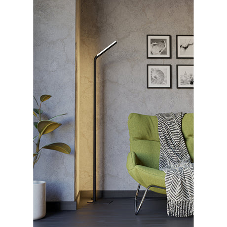 Mirante LED Floor Lamp in black, slim steel and aluminium pole with angled bar-shaped head on a flat base, shown beside a green armchair in a living room.