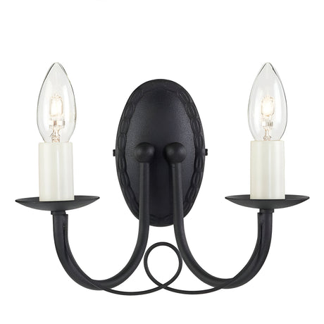 The Minster 2 Light Wall Light - Black is a sophisticated wall sconce featuring two candle-shaped bulbs on gracefully curved arms, each enclosed in clear glass. It includes an oval backplate and cream-colored holders that resemble candles, making it a perfect fit for both contemporary and classic interiors.