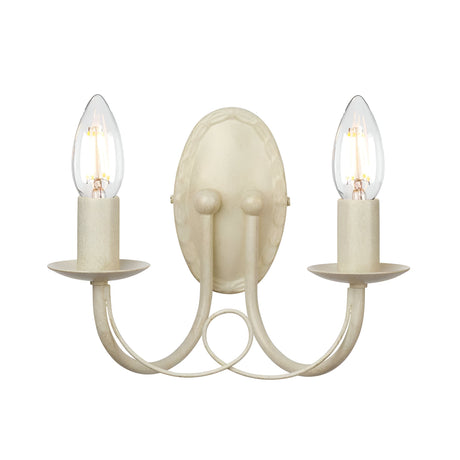 The Minster 2 Light Wall Light in ivory and gold patina is a vintage-style, wall-mounted fixture featuring two exposed E14 bulbs. Its beige frame offers a curvy, symmetrical shape and round base, with a subtle gold patina enhancing its elegance.